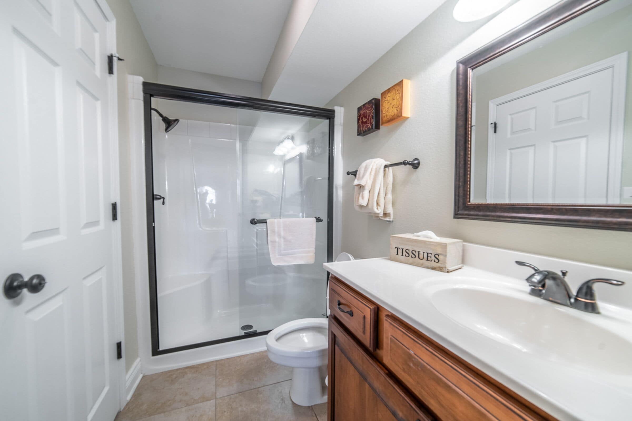 A bathroom with a glass-enclosed shower, a white toilet, a sink with a mirror, and wooden cabinetry.