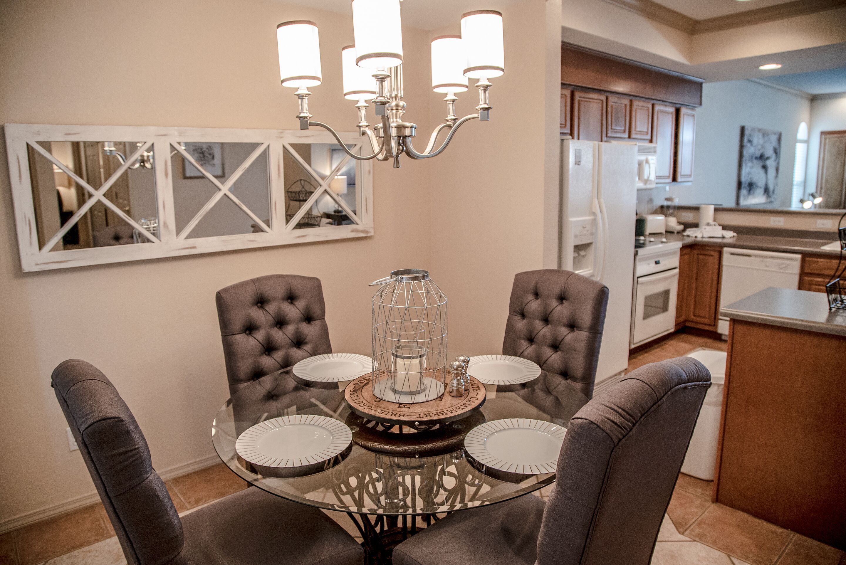 A dining area with a glass table surrounded by cushioned chairs, a chandelier, and a decorative centerpiece.