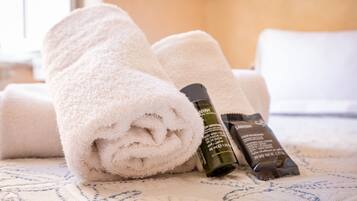 Neatly folded white towels and two toiletries on a bed with a patterned bedspread.
