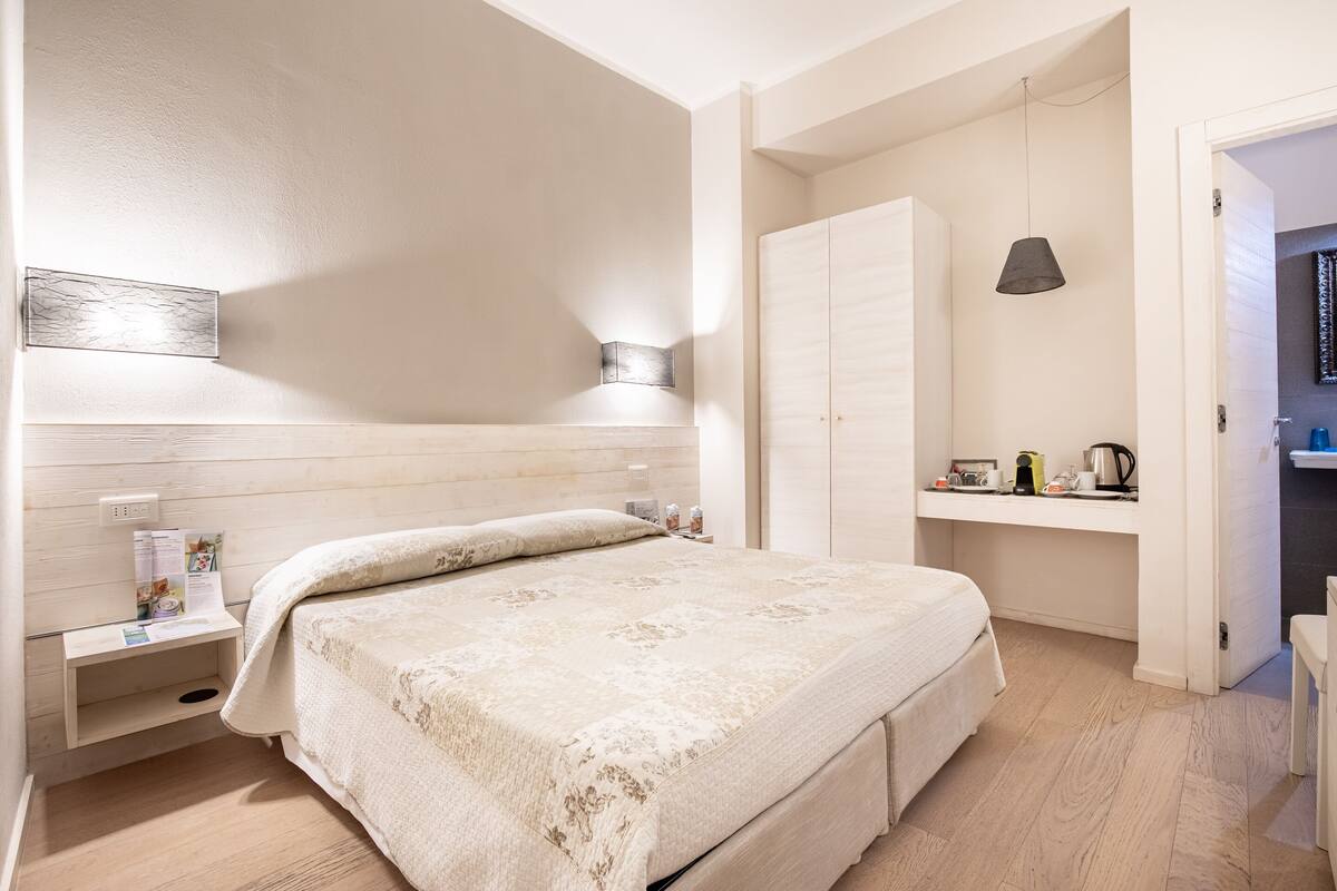 A bedroom with a bed, bedside table, lamp, wardrobe, and a small shelf with items.