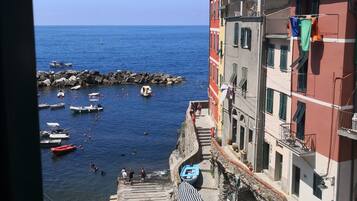 A coastal town with boats docked along the shore, a stone staircase leading to a building, and a clear blue sky.