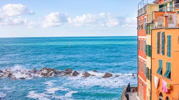A coastal scene with a rocky shoreline, a clear blue sea, and colorful buildings with balconies.