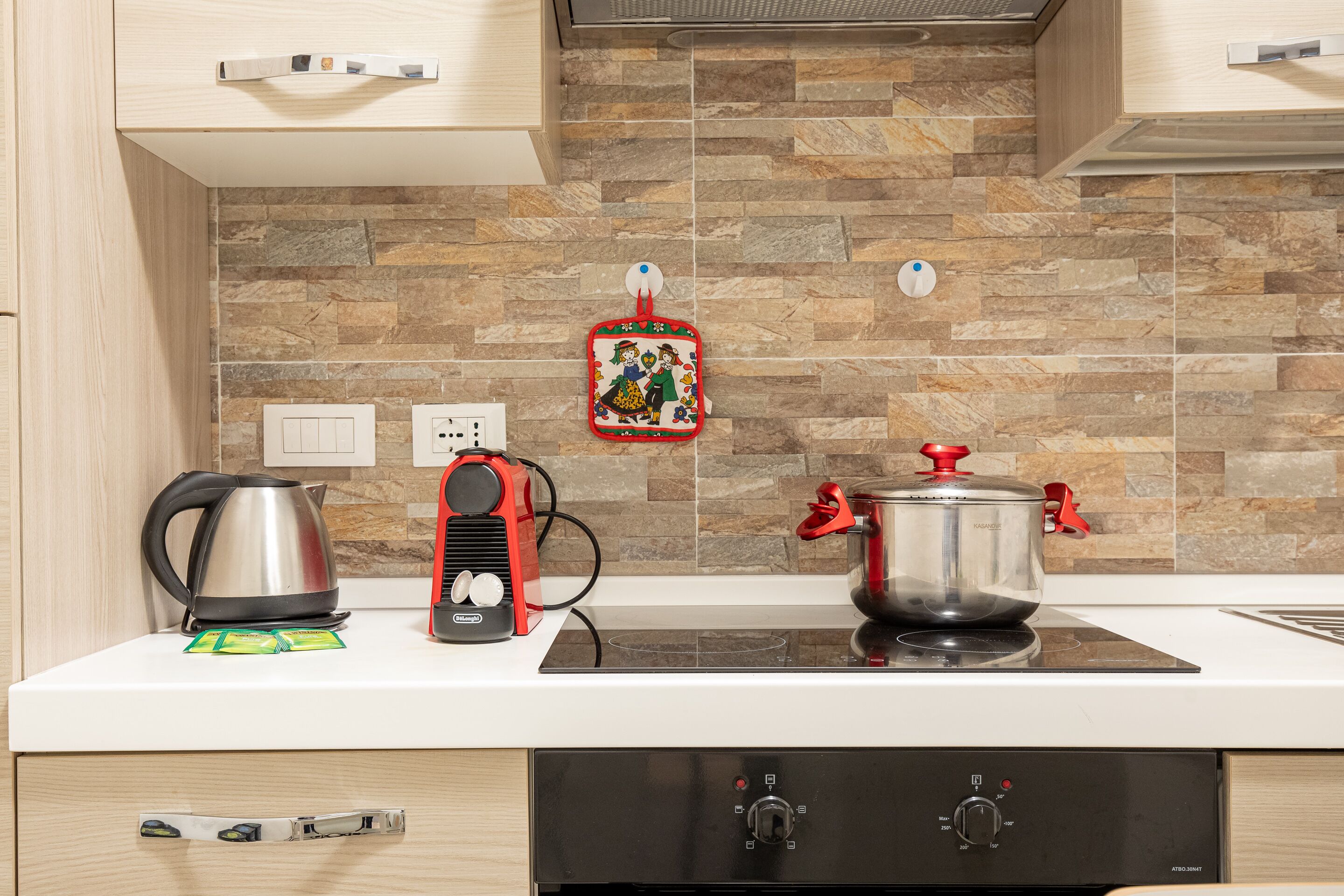 Una cocina con protector contra salpicaduras de piedra, un hervidor, un hervidor eléctrico rojo y una olla sobre una cocina de inducción.