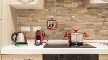 Una cocina con protector contra salpicaduras de piedra, un hervidor, un hervidor eléctrico rojo y una olla sobre una cocina de inducción.