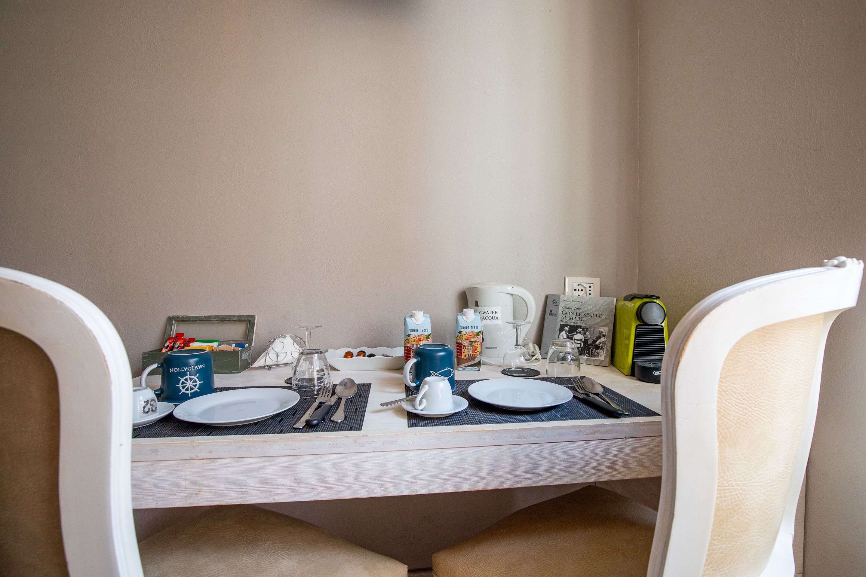 Une table mise pour le petit-déjeuner, avec de la vaisselle, des couverts, une bouilloire et une machine à café, préparée pour deux personnes.