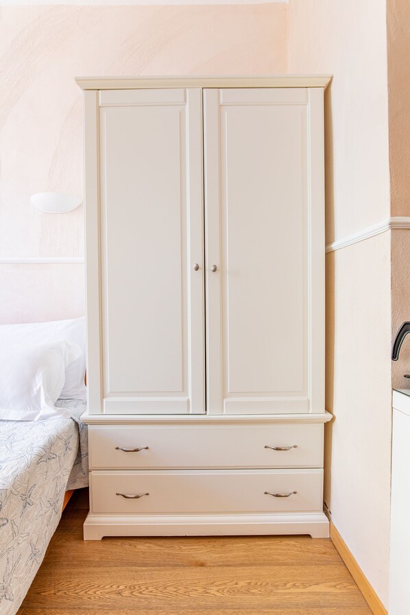 A white wardrobe with two doors and two drawers, positioned next to a bed with a white and blue patterned bedspread. - Alla Marina Affittacamere (Riomaggiore)