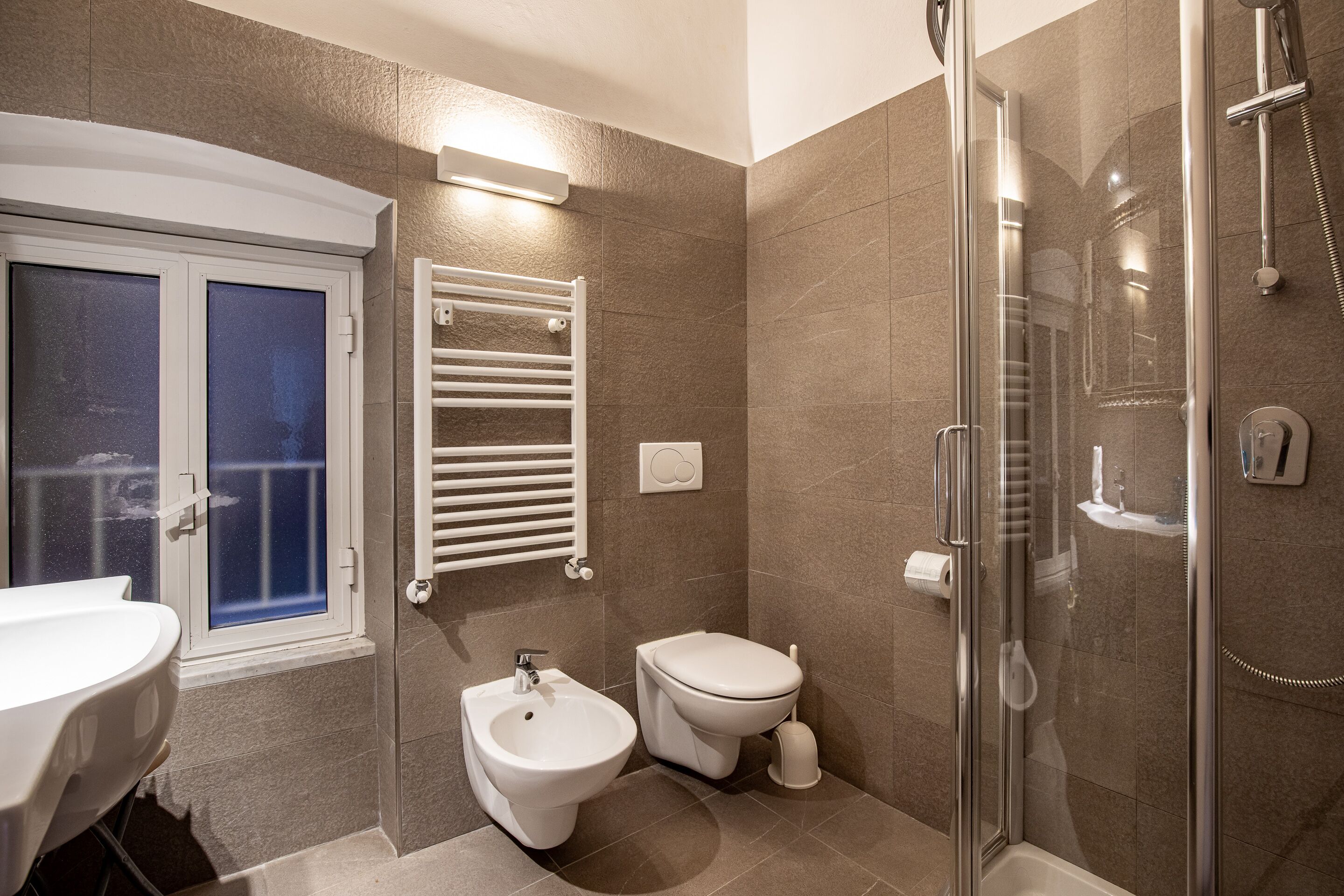 A modern bathroom with a bidet, toilet, and glass-enclosed shower.