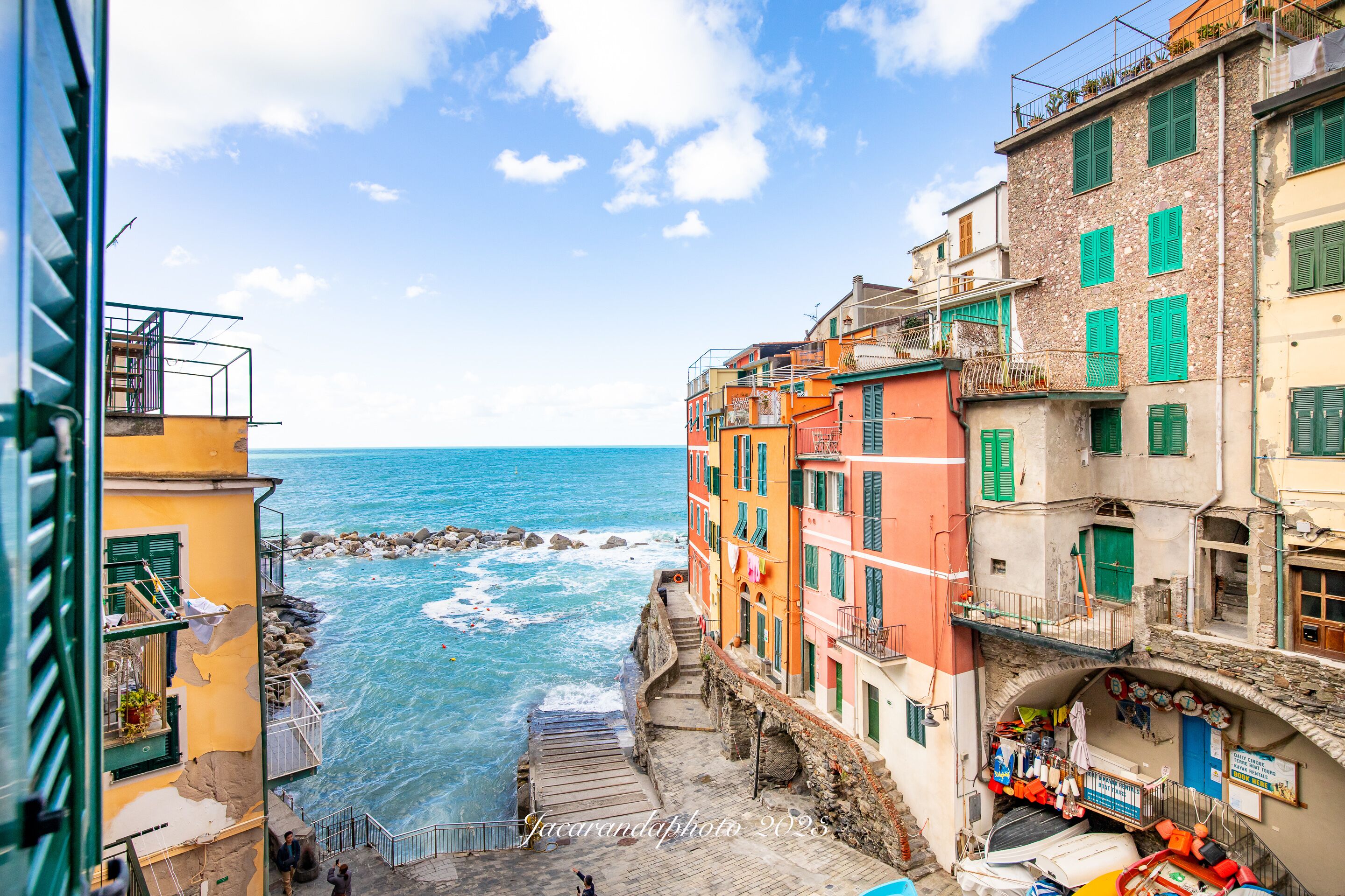Un pueblo costero con edificios coloridos, una escalera de piedra que baja a la playa y una vista despejada del mar.