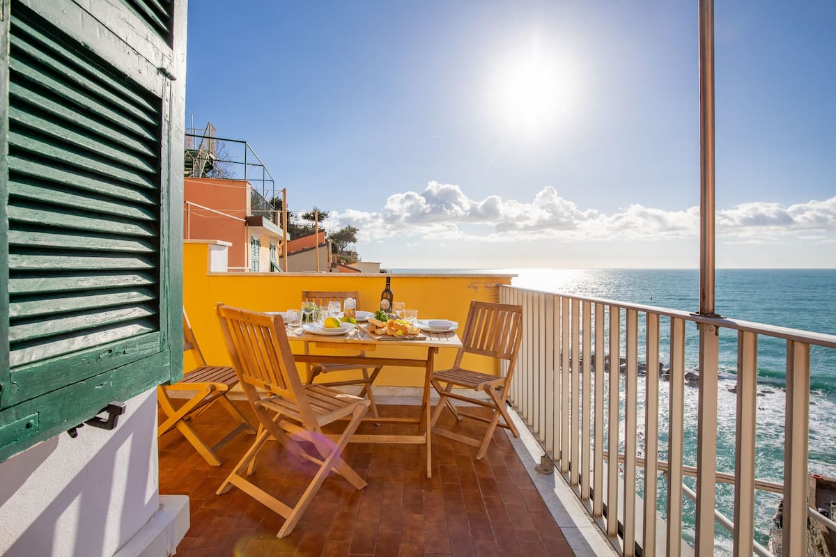 A balcony with a table set for two, overlooking a coastal view.