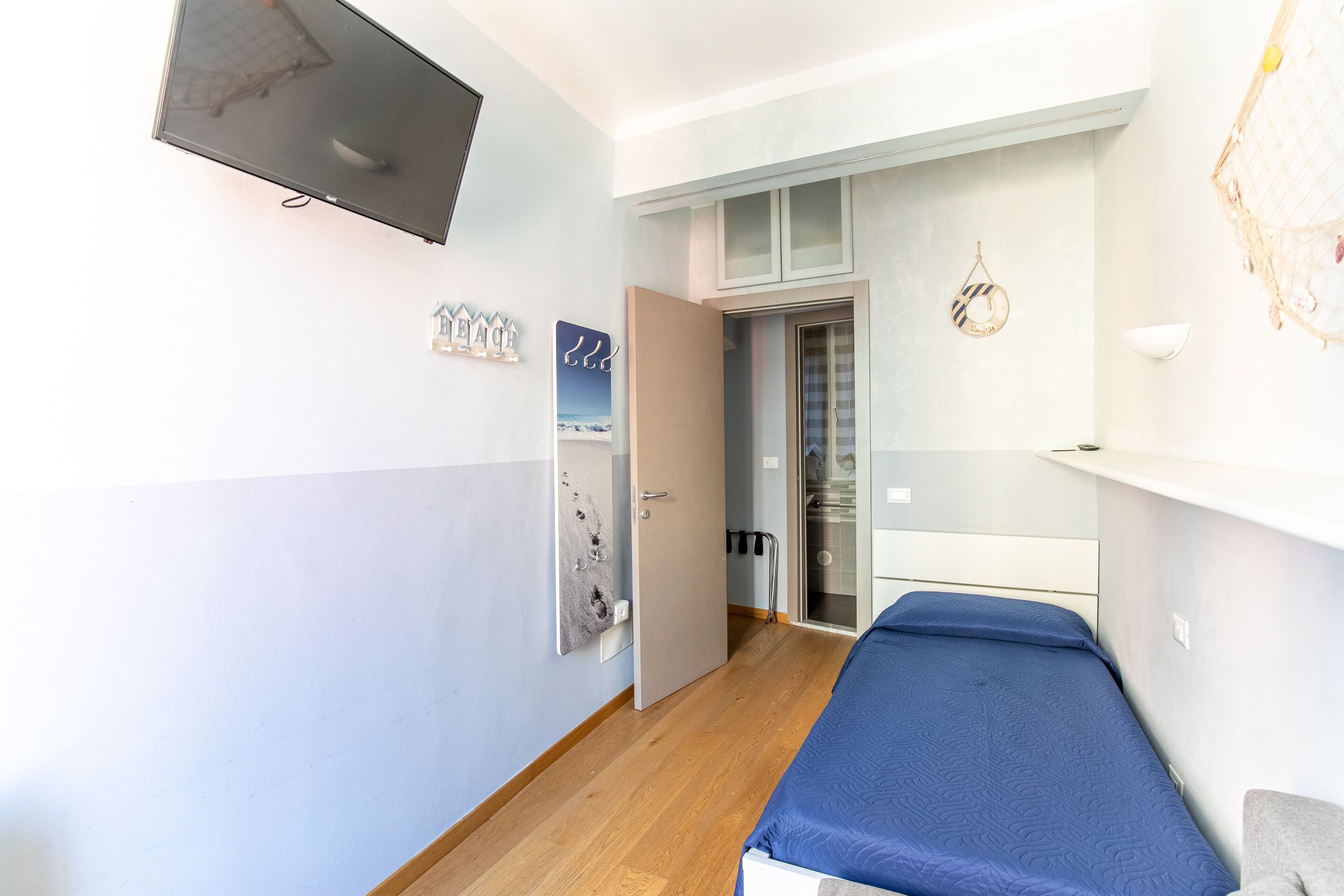 Ein Zimmer mit einem Bett, einem an der Wand befestigten Fernseher und einer Tür zu einem anderen Raum.
