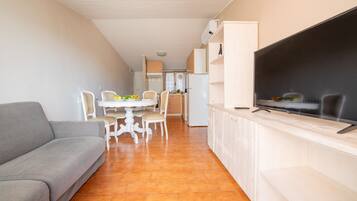 A compact living space with a sofa, dining table, chairs, a TV, and a kitchen area.
