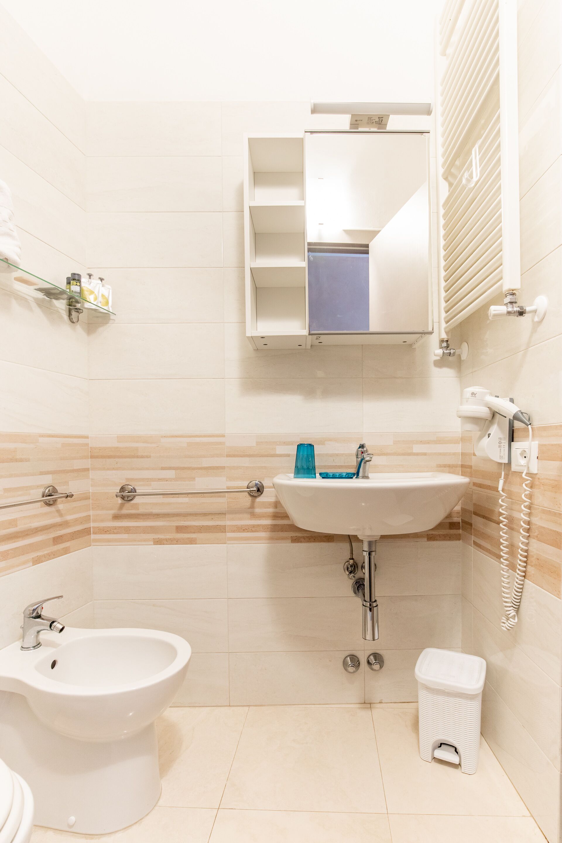 A bathroom with a white sink, a bidet, a small trash bin, and a toilet.