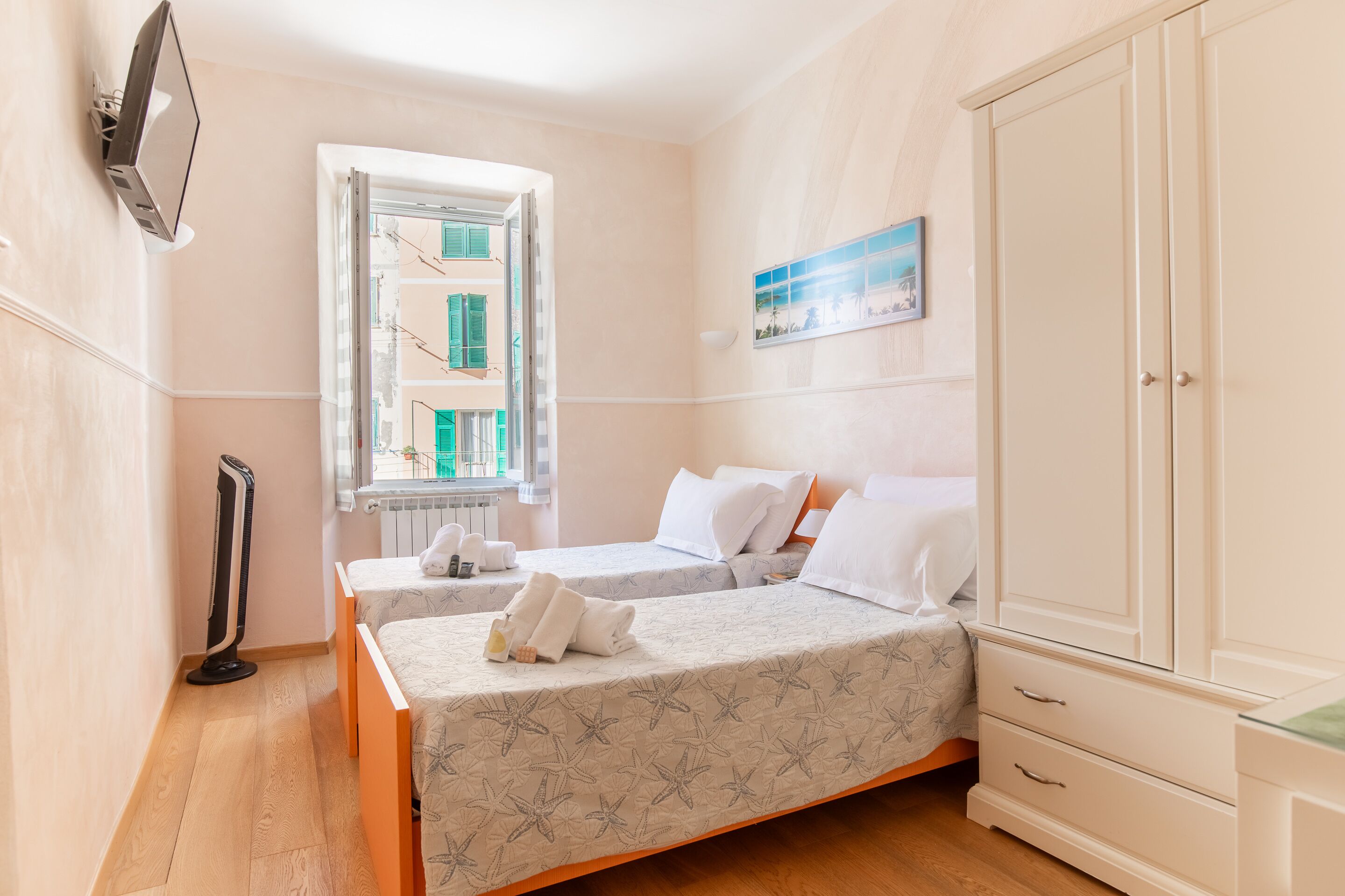 Une chambre avec deux lits, une armoire, un radiateur et un téléviseur fixé au mur.