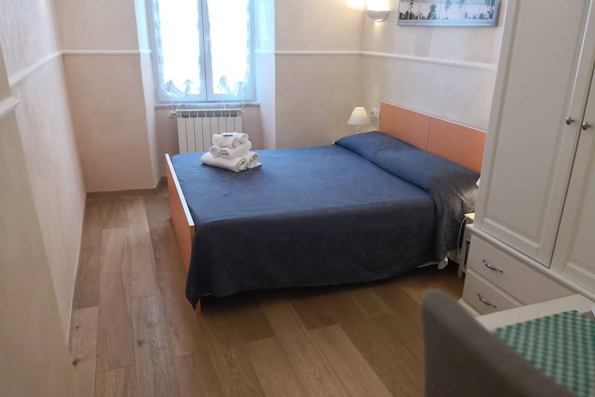 A bedroom with a bed, a radiator, a window, and a bedside table with a lamp.