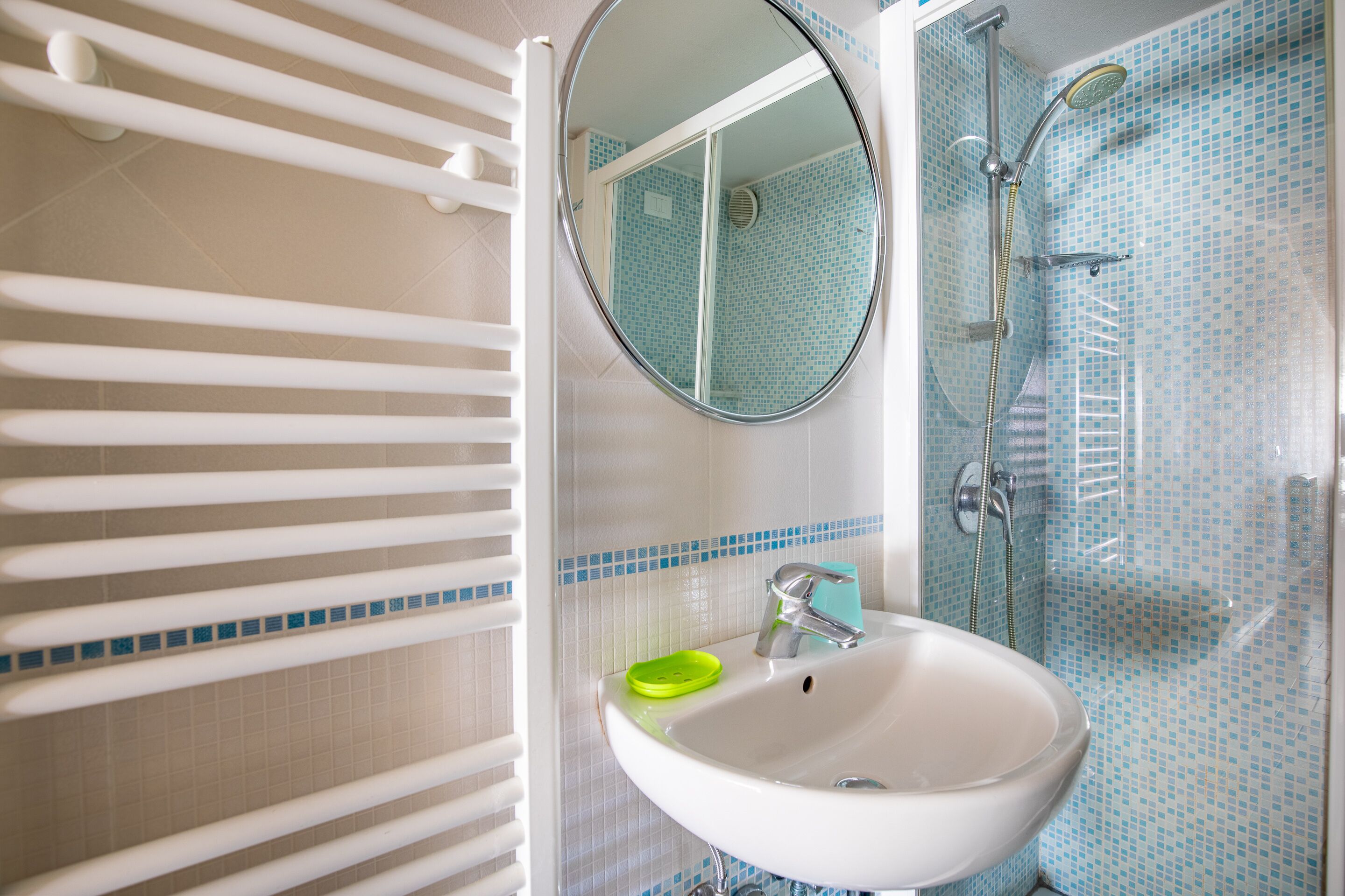 A bathroom with a white sink, a mirror, and a shower with blue mosaic tiles.