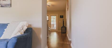A hallway with a blue couch, wooden flooring, and a door leading to a room with a window.