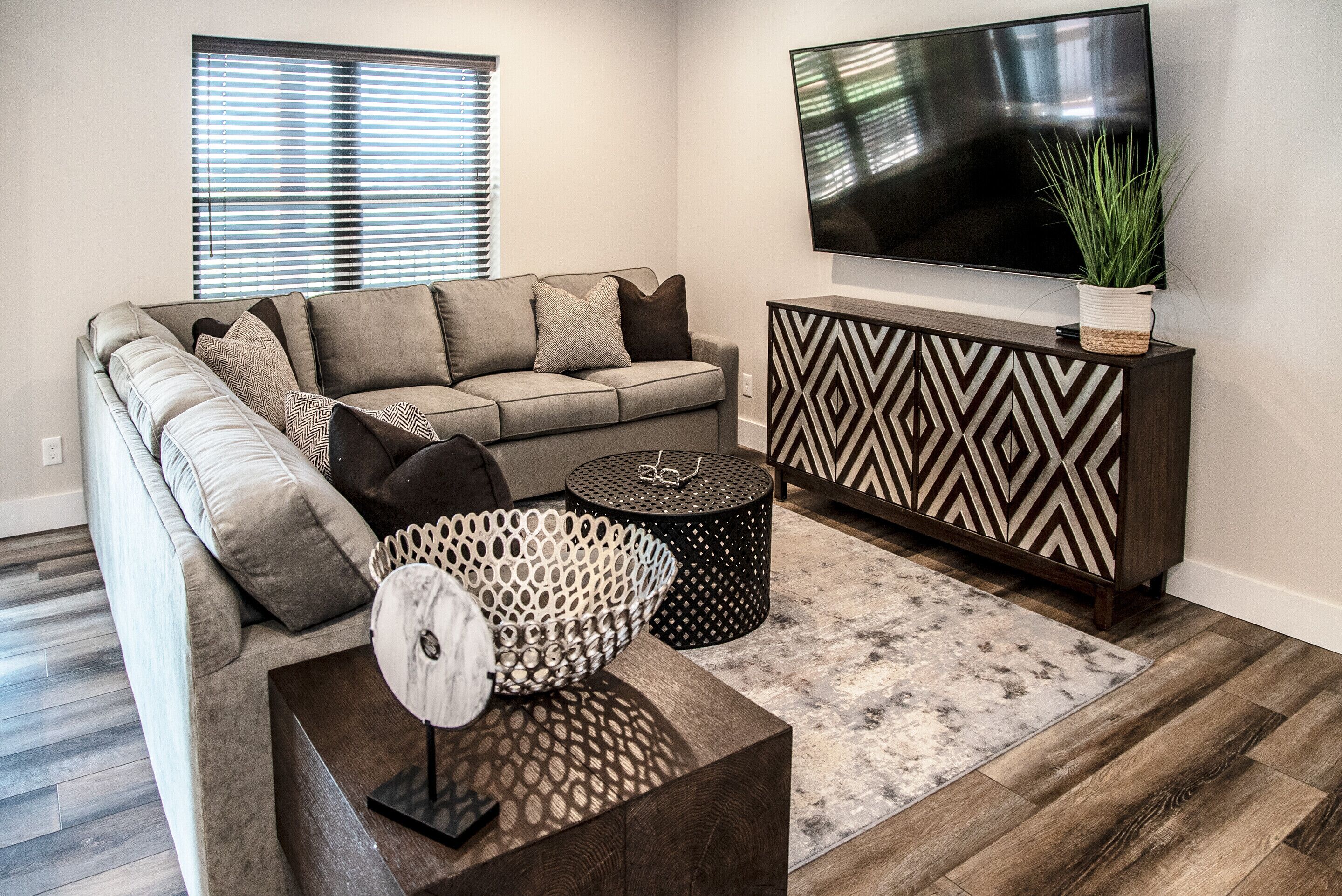 A modern living room with a sectional sofa, a flat-screen TV, a decorative console, and a patterned rug.