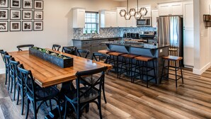 A modern kitchen with white cabinets, a central island, bar stools, and a dining area with a wooden table and chairs. - Reunion Lodges at Thousand Hills (Branson)