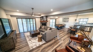 A spacious living room with a gray sofa, wooden flooring, a fireplace, and a dining area with a table and chairs. - Reunion Lodges at Thousand Hills (Branson)