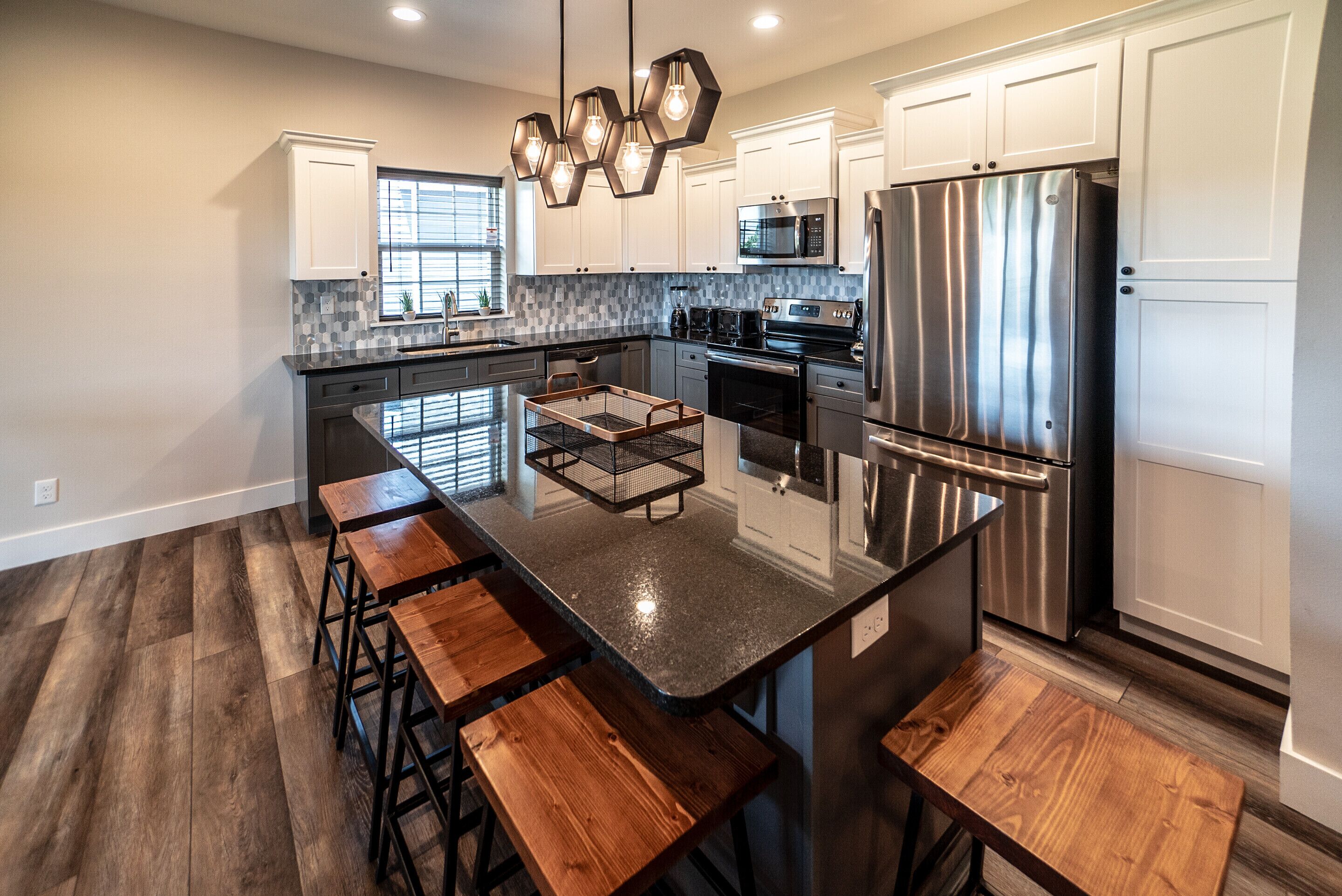 A modern kitchen with a central island, bar stools, stainless steel appliances, and a backsplash.