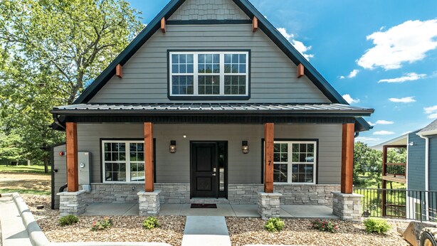 A two-story house with a gabled roof, stone foundation, and a front porch with columns. - Reunion Lodges at Thousand Hills (Branson)