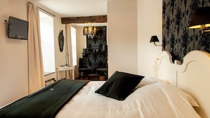 A neatly made bed with a black pillow and a white comforter, a television on the wall, a chandelier, and a patterned wallpaper. - Hotel Le Saint Hadelin (Houyet)