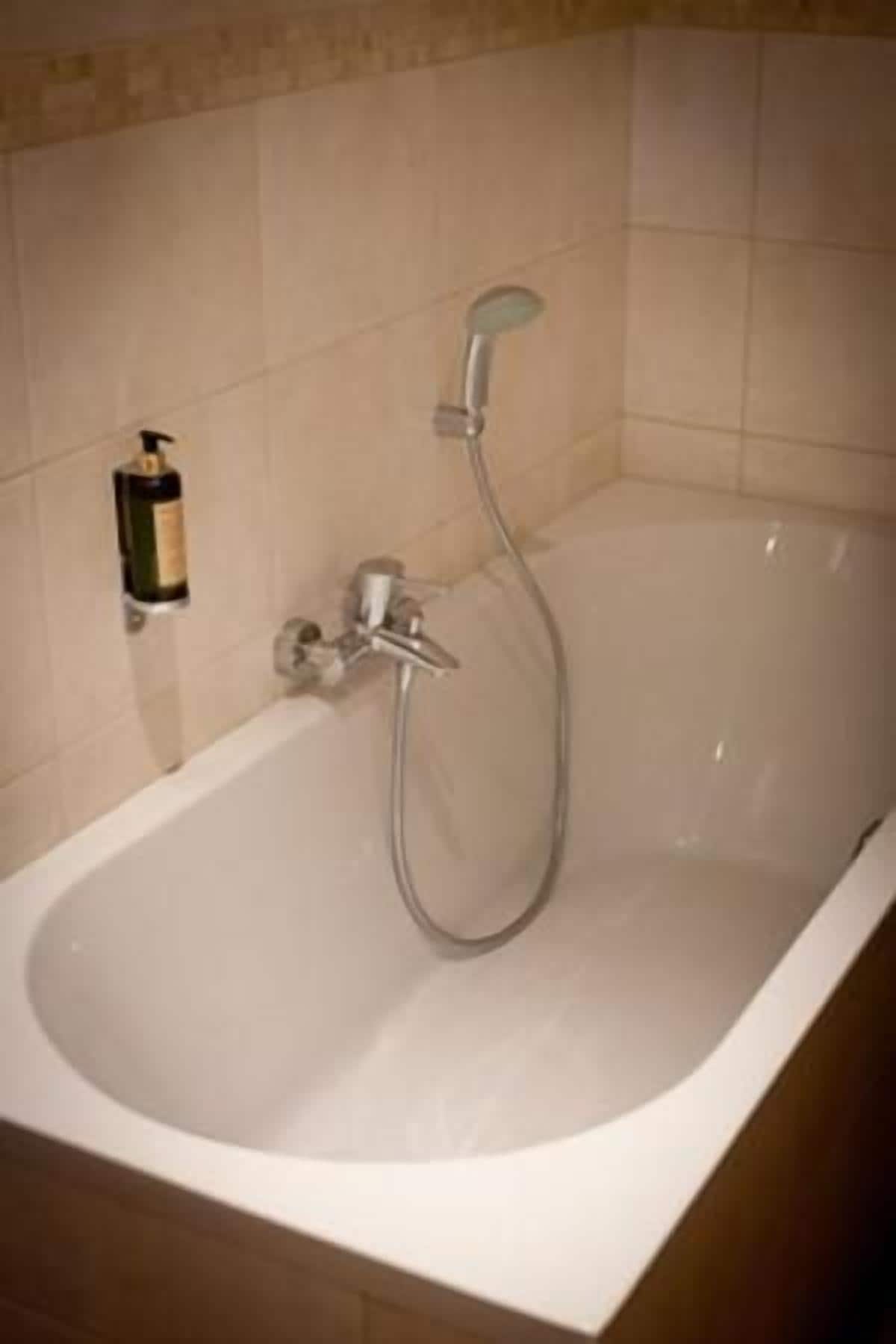 Een badkuip met een handdouche en een fles shampoo aan de muur.