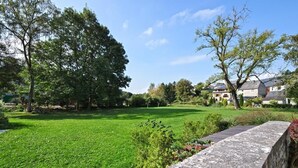 A well-maintained grassy area with a stone wall and trees, likely part of a residential property. - Hotel Le Saint Hadelin (Houyet)