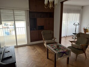 Un salon spacieux doté d’un parquet en bois à motifs en chevrons, d’un fauteuil à motifs, d’un canapé assorti et d’une table agrémentée d’un chemin de table coloré.