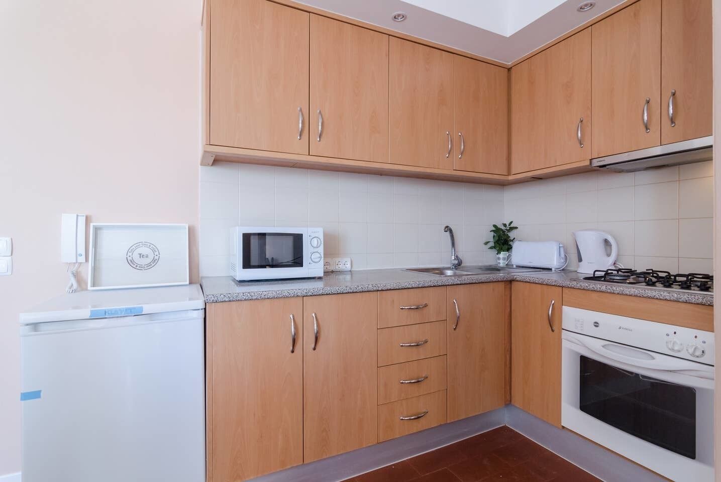 A compact kitchen with wooden cabinets, a microwave, a stove, and a refrigerator.