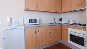 A compact kitchen with wooden cabinets, a microwave, a stove, and a refrigerator. - Remarkable 2-Bed Apartment (ALVOR, Algarve)