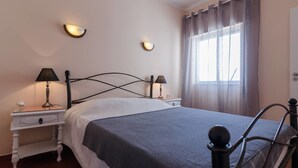 A neatly arranged bedroom with a bed, two bedside tables with lamps, a window with curtains, and a door. - Remarkable 2-Bed Apartment (ALVOR, Algarve)