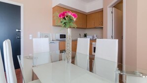 A modern kitchen with wooden cabinets, a microwave, and a coffee maker. There is a dining table with chairs and a vase with flowers. - Remarkable 2-Bed Apartment (ALVOR, Algarve)