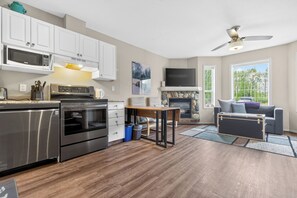 A modern kitchen with stainless steel appliances, a dining area with a table, and a living room with a sofa and a fireplace.