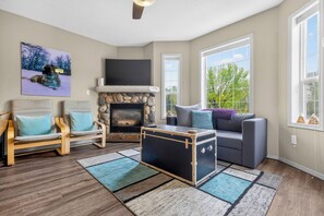 A living room with a stone fireplace, a television mounted above it, a sofa, a wooden chair, and a rug. - 5 Mins to the Resort & Fernie. On the Elk River (Fernie)