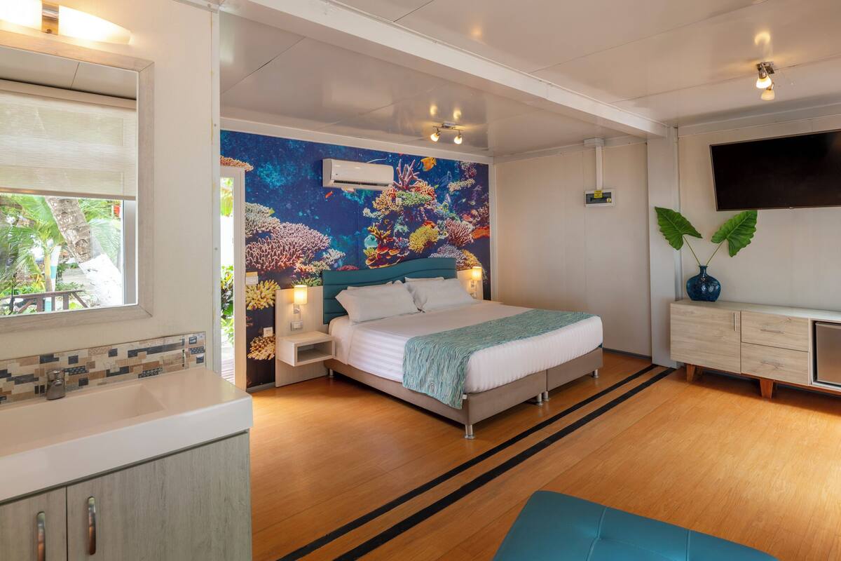 Ein modernes Schlafzimmer mit Bett, Wandgemälde, Fernseher und einem Badebereich.