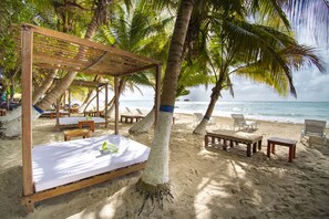 A beach cabana with a wooden bed and lounge chairs, surrounded by palm trees and overlooking the ocean. - Hotel Reina del Mar By Dorado (San Andrés)