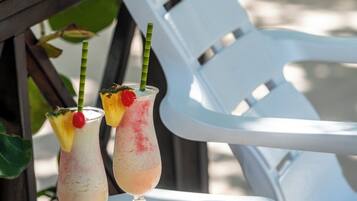 Two drinks with fruit garnishes on a table, a plate of fruit, and a white plastic chair.