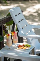Dos bebidas con adornos de frutas sobre una mesa, un plato de fruta y una silla de plástico blanca.