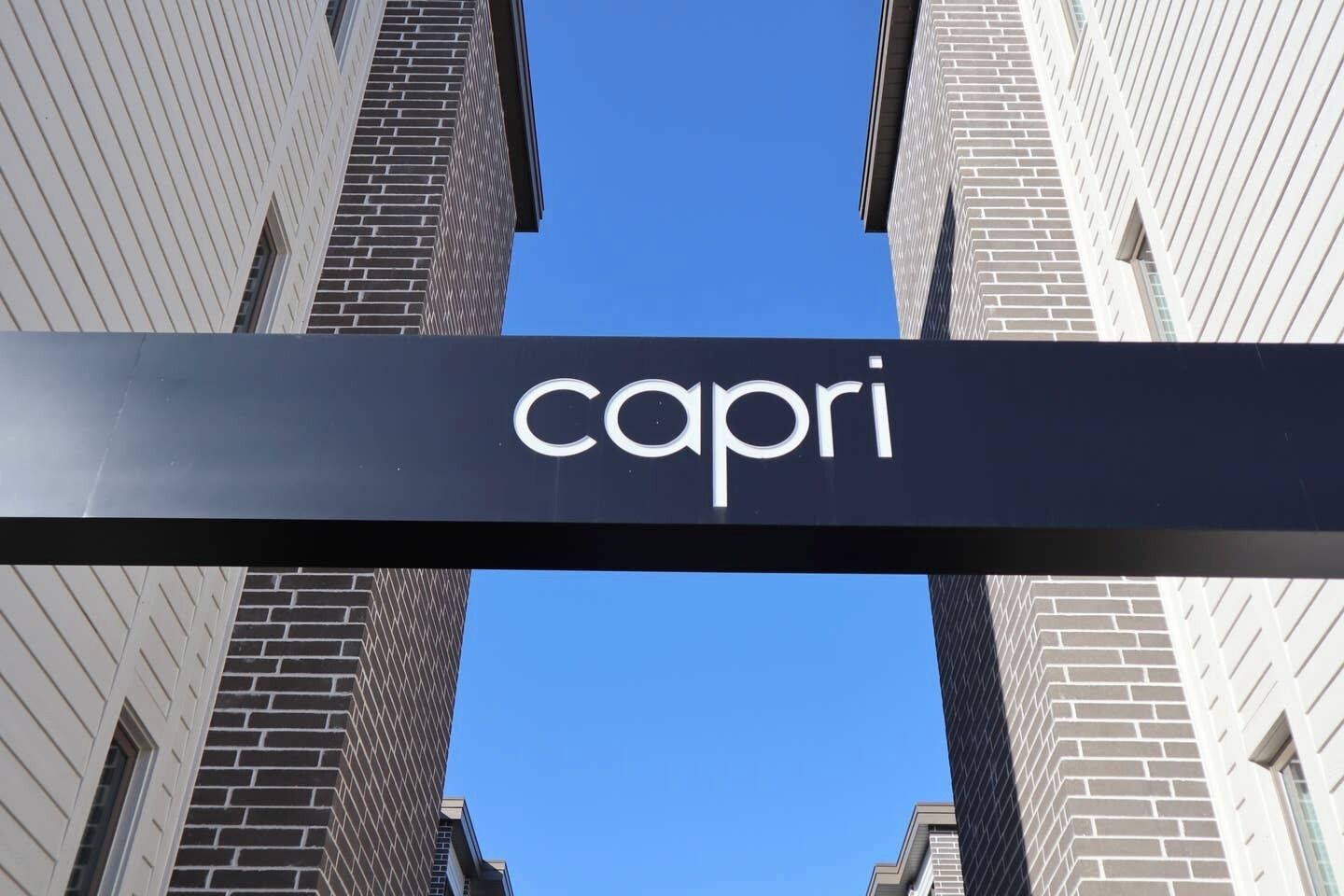 Et skilt med ordet "capri" mod en klar blå himmel, indrammet af høje bygninger.