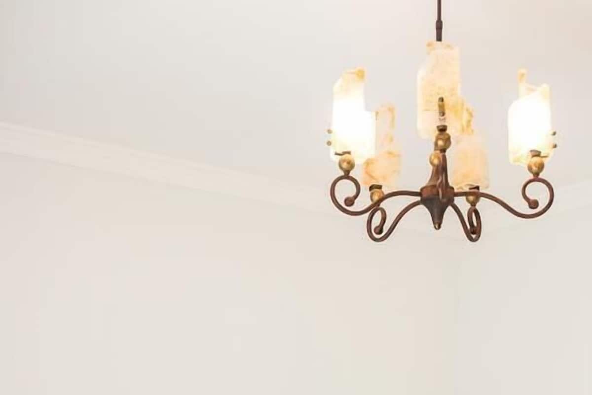 A neatly made bed with a blue bedspread and white pillows, a black nightstand with a lamp, and a chandelier above.