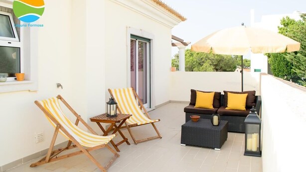 A balcony with two striped lounge chairs, a sofa with yellow cushions, and a table with a lantern. - Laguna Formosa - Holidays in the Algarve (Faro)