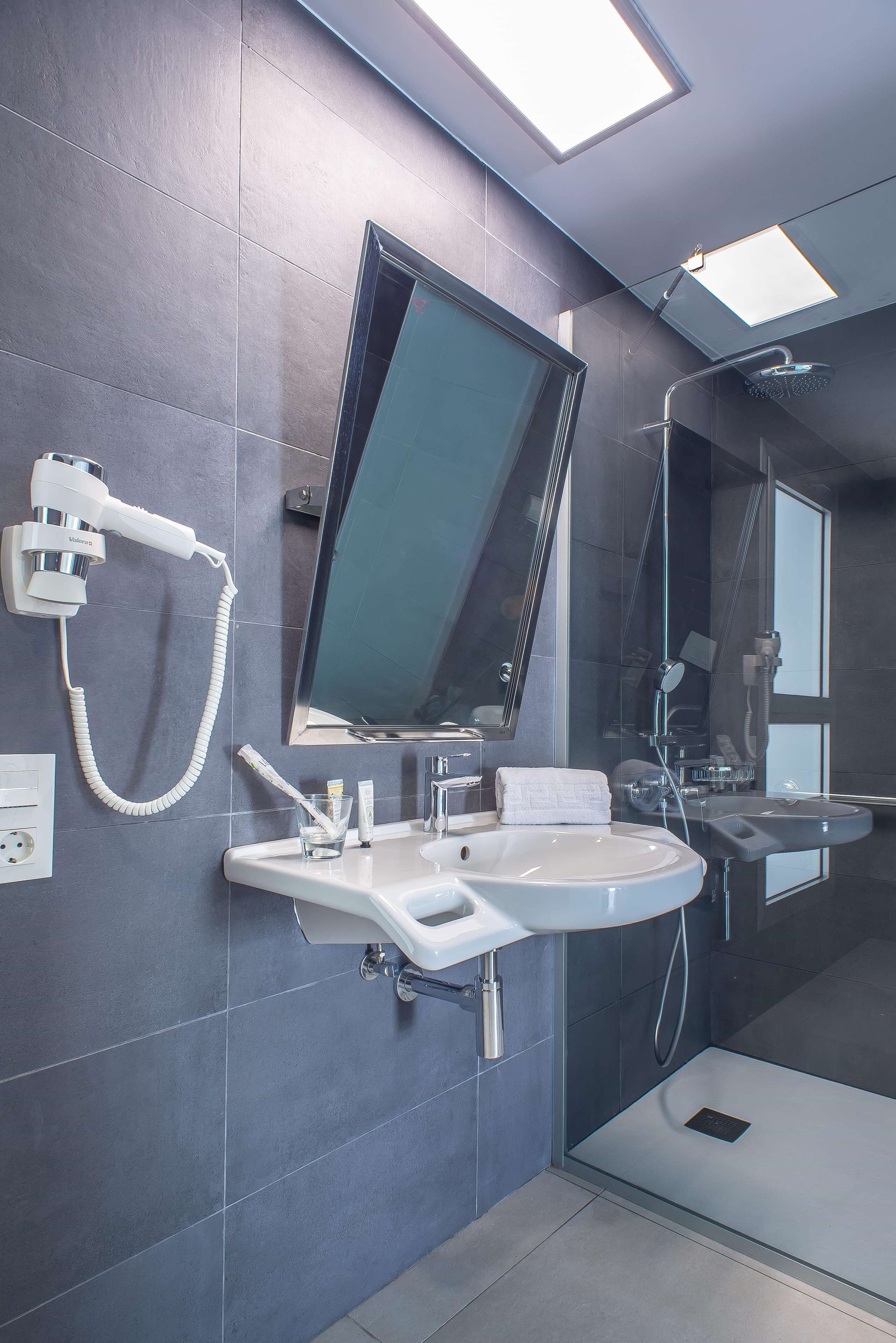 Une salle de bain moderne équipée d’un grand miroir, d’un sèche-cheveux, d’un lavabo et d’une douche.