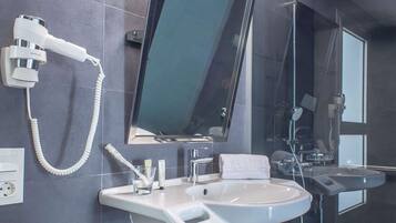 Une salle de bain moderne équipée d’un grand miroir, d’un sèche-cheveux, d’un lavabo et d’une douche.