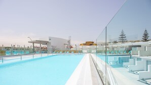 Una piscina con agua cristalina, rodeada de sillones de descanso y un edificio moderno al fondo.