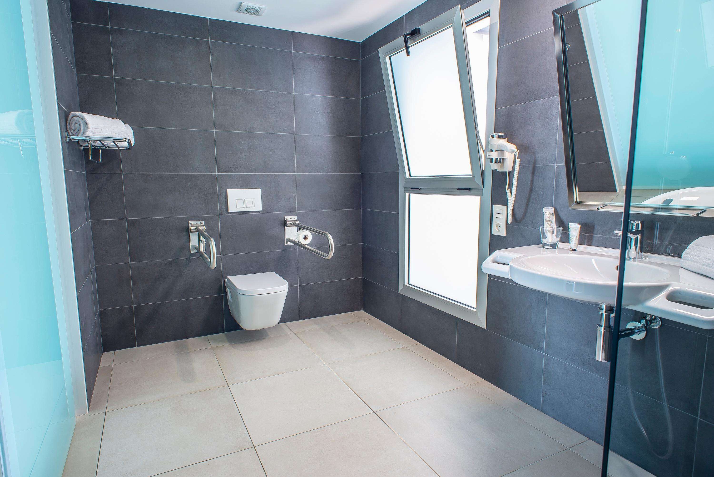 Ein modernes Badezimmer mit dunklen Fliesen, einer Toilette, einem Waschbecken und einer Duschkabine.