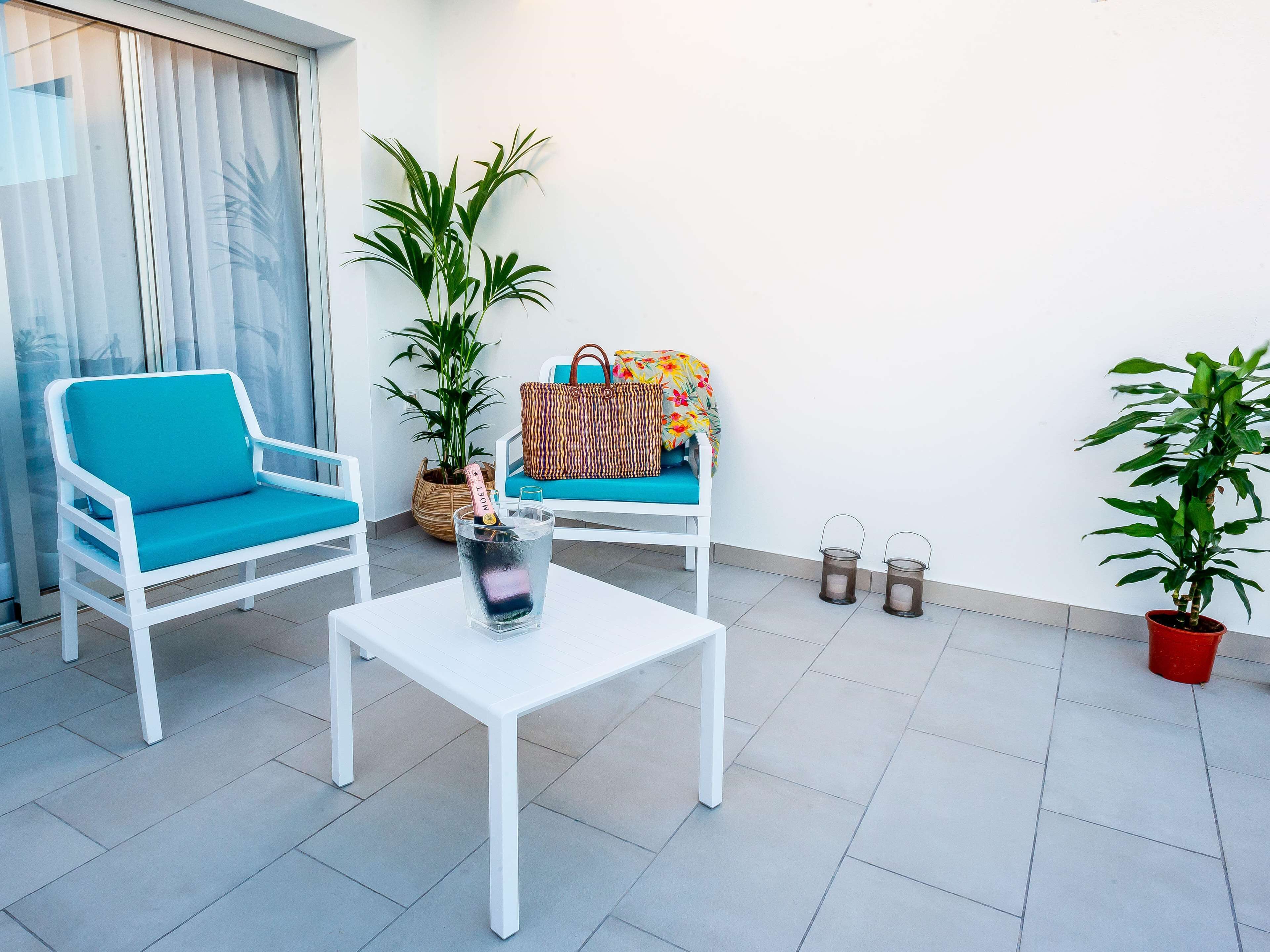 Un área de estar al aire libre y de diseño moderno, con dos sillas blancas, una mesita pequeña y plantas en macetas.