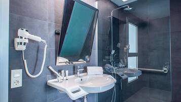 Un baño moderno con un espejo grande, un lavamanos, un cabezal de ducha manual y una ducha con mampara de vidrio.