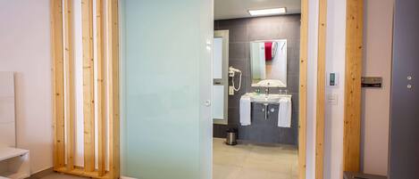A modern hotel room with a sliding door leading to a bathroom. The room features a bed, a bedside table, and a red accent wall.