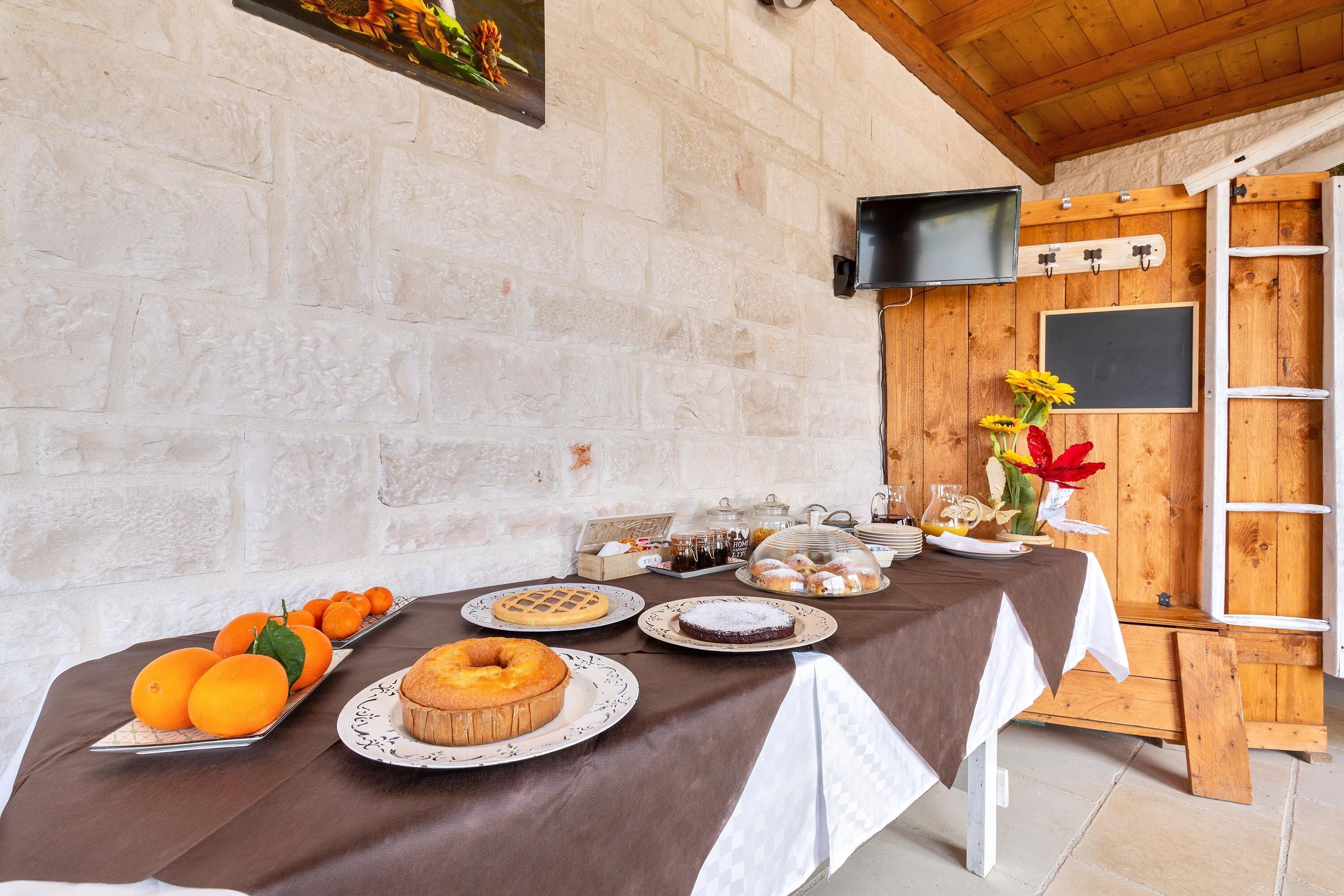 Ein Frühstücksbuffet mit verschiedenen Backwaren und Früchten auf einem Tisch, vor einer rustikalen Steinwand mit Holzbalkendecke.
